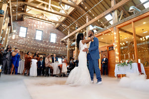 An image of a bride and groom dancing on a smoke covered floor in front of a crowd of people at tables at Boston Harbor Distillery. Photograph by Q.H. Concept