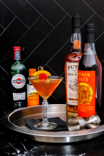Some Like It Hot Manhattan pictured with bottles of Putnam Rye Whiskey, Demon Seed, Orange Bitters and Vermouth