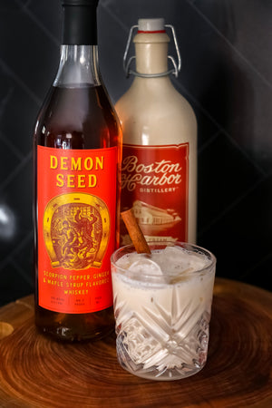 Cream N' Demon cocktail with cinnamon stick in front of bottles of Demon Seed and Boston Harbor Distillery Maple Cream