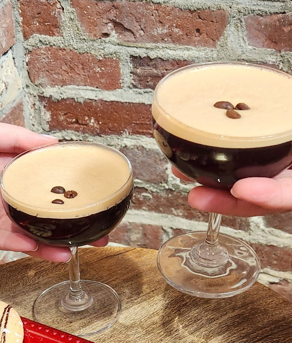 An image of two people holding espresso martinis in front of a brick wall