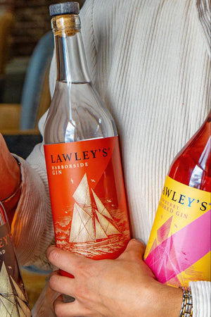 An image of a person holding in one arm a bottle of Lawley's Harborside Gin and Lawley's Strawberry Gin