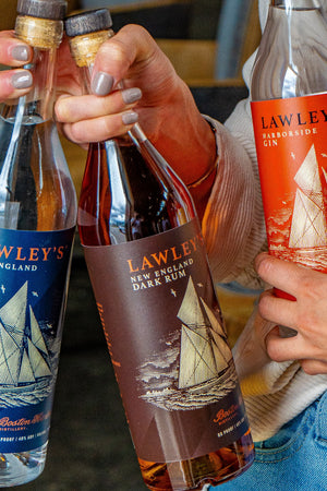 An image of a person holding in one hand a bottle of Lawley's Light Rum and Lawley's Dark Rum and in their other hand a bottle of Lawley's Harborside Gin.